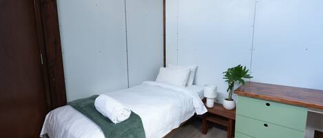 A bedroom with a bed, bedside table, green dresser, and a potted plant.