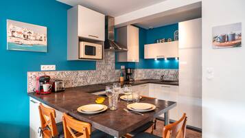 A modern kitchen with a dining table set for four, equipped with a coffee machine, wine glasses, and a toaster.