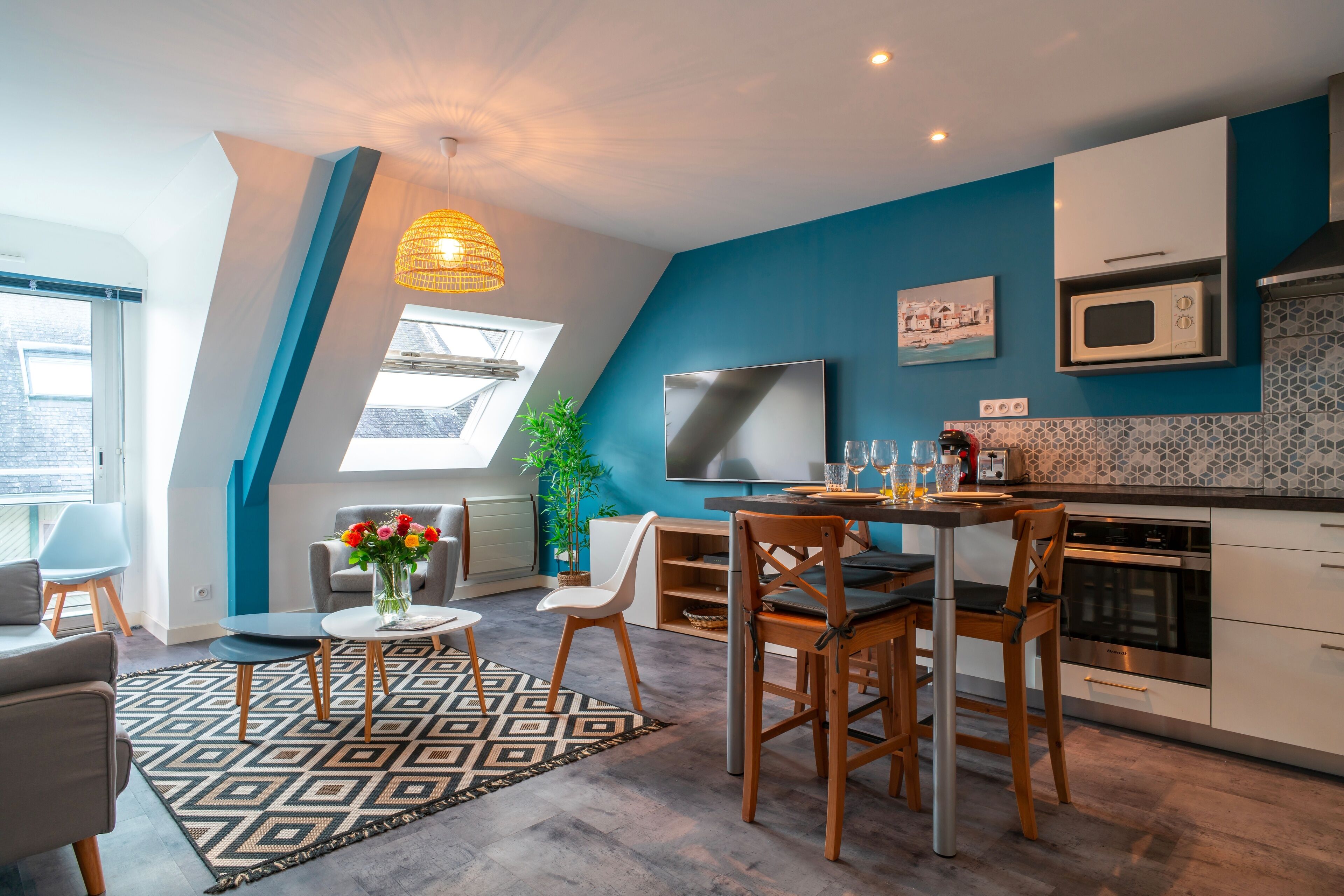 A modern kitchen with a dining area, featuring a large window, a microwave, and a dining table with chairs.
