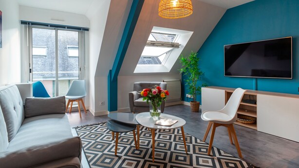 Una sala de estar moderna con un sofá, dos sillones, una mesa de centro, un televisor y un ventanal con vistas al exterior.