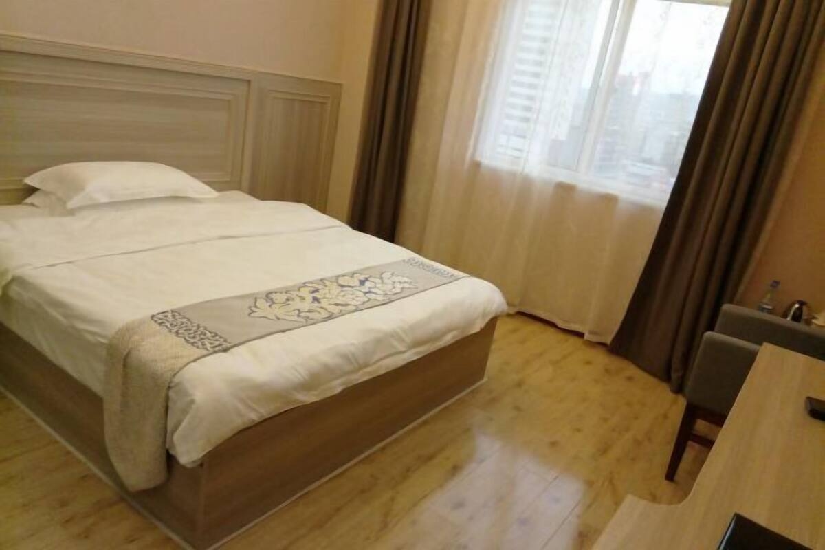 A hotel room with a wooden bed, a desk, and a window with curtains.
