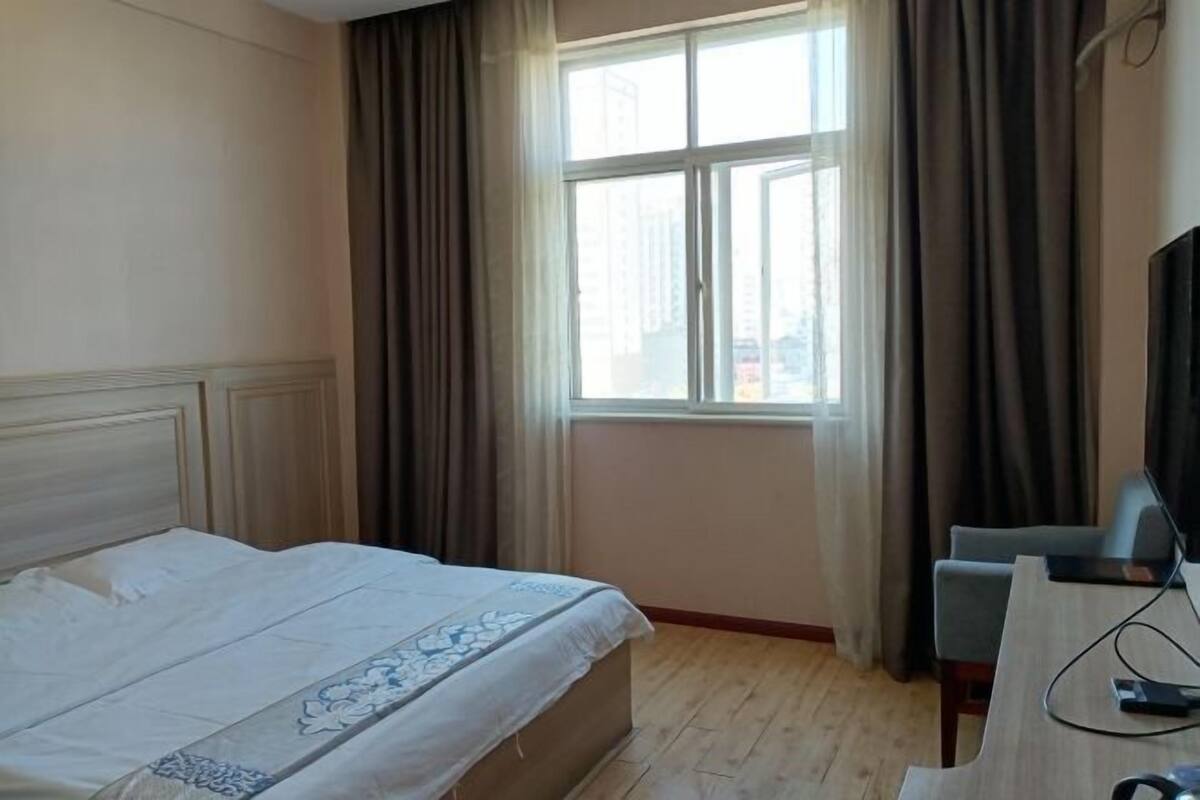 A hotel room with a bed, a desk with a computer, and a window with curtains.