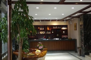 A reception area with a wooden counter, a potted plant, and a bar area with shelves of bottles.