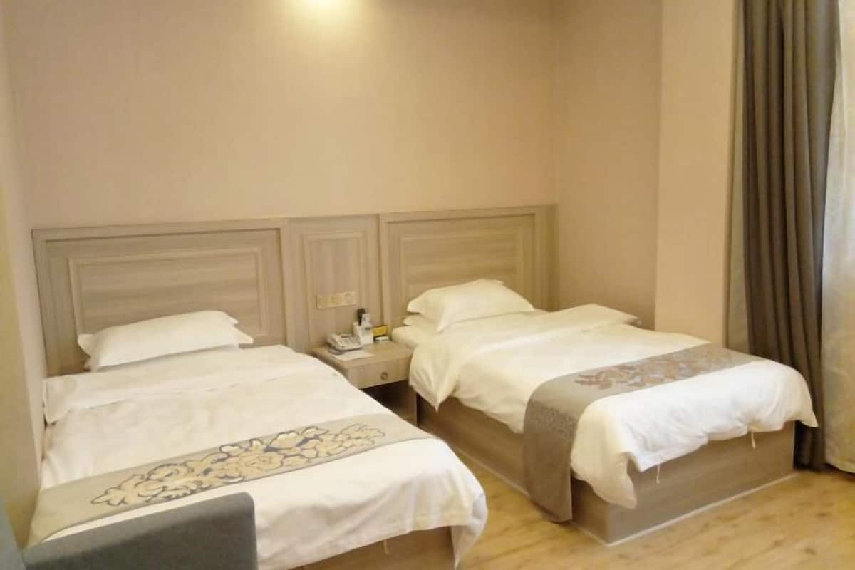 A hotel room with two beds, a nightstand, and a lamp.