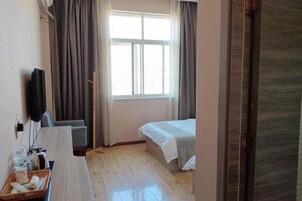 Quarto de hotel com cama, escrivaninha com cadeira, televisão e janela com cortinas.