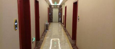 A hotel hallway with doors on both sides, a marble floor, and an emergency exit sign at the end.
