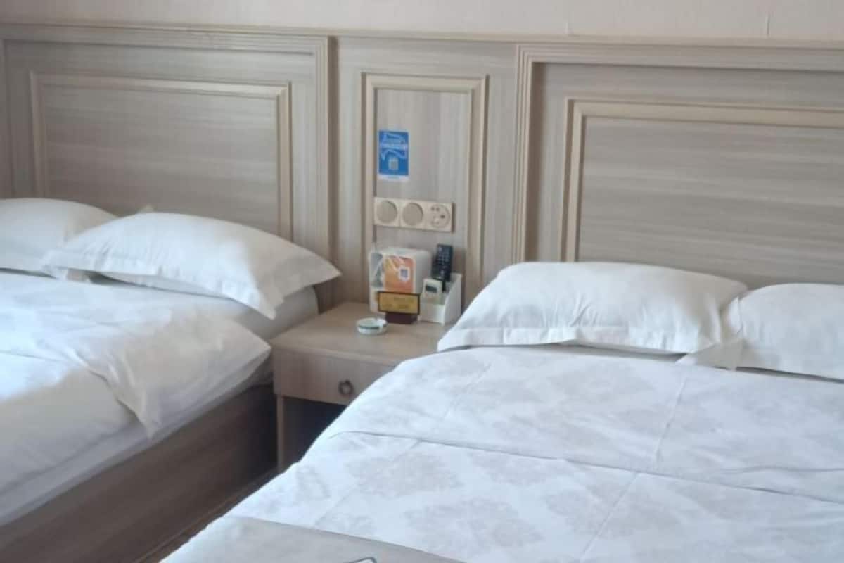A hotel room with two beds, a nightstand, and a wall-mounted control panel.