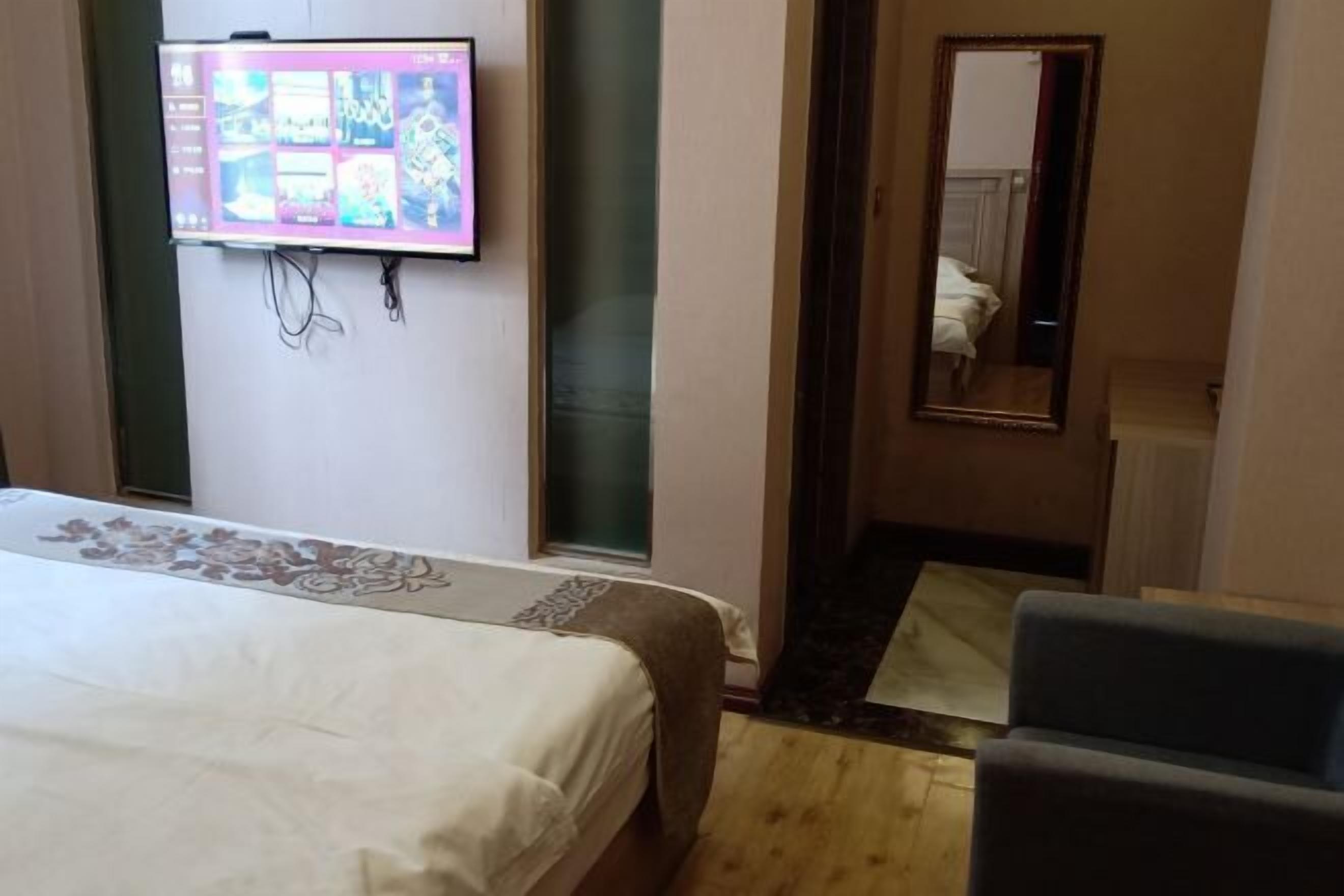 A hotel room with a bed, a television mounted on the wall, a mirror, and a chair.