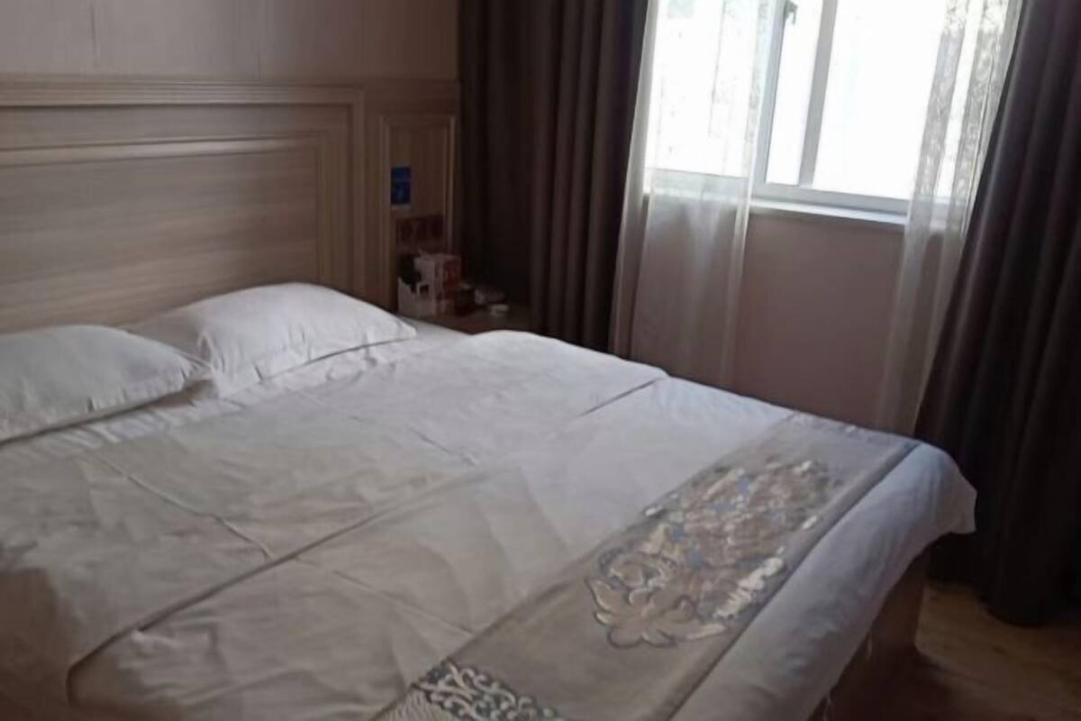 A hotel room with a large bed, a wooden headboard, and a window with curtains.
