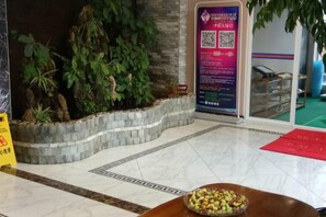 A reception area with a marble floor, a plant wall, a QR code sign, and a bowl of fruit on a table. - Chuxiong Haiheng Hotel (Chuxiong City)