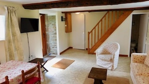Ein Wohnzimmer mit einer Holztreppe, einem an der Wand montierten Fernseher, einem Esstisch mit Stühlen und einem Sofa.