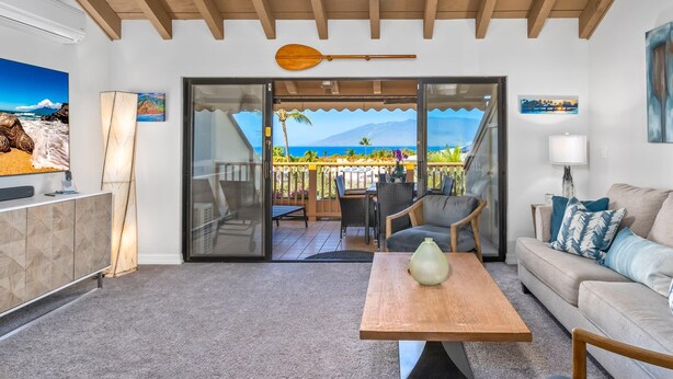 A living room with a sofa, a coffee table, and a view of the ocean through a sliding glass door. - Luxurious & Spacious Ocean Vistas (Wailea-Makena)