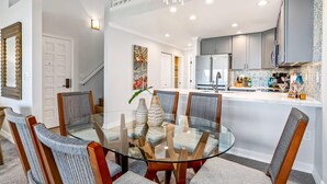 A modern kitchen with a central island, a dining area with a glass table, and a staircase leading to another level. - Luxurious & Spacious Ocean Vistas (Wailea-Makena)