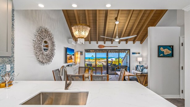 A modern kitchen with a large island, wooden ceiling beams, and a view of the outdoors. - Luxurious & Spacious Ocean Vistas (Wailea-Makena)