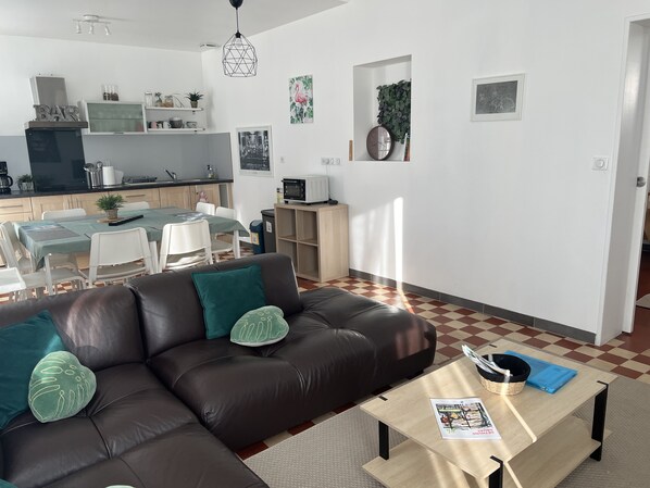 A modern living room with a brown leather sofa, a coffee table, and a dining area with a table and chairs.