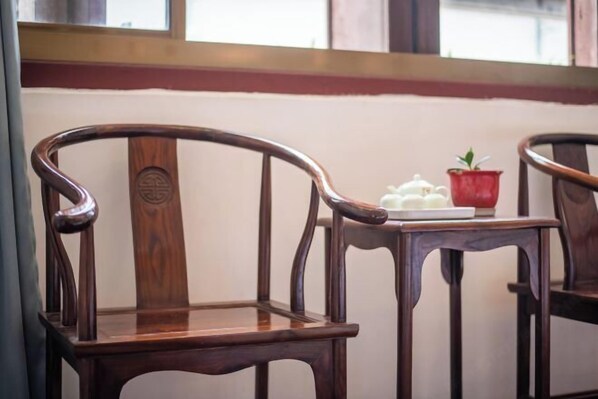 Une chaise en bois dotée d’un dossier incurvé et d’un accoudoir en métal, placée à côté d’une petite table sur laquelle se trouvent une théière blanche et un pot rouge.
