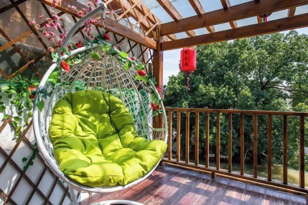 Una silla colgante con un cojín verde, una barandilla de madera y un farol rojo.