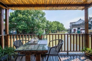 Una terraza de madera con una mesa y sillas, con vistas a un edificio tradicional y árboles.