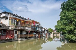Une ville chinoise traditionnelle construite sur l’eau, avec des bâtiments à plusieurs étages le long d’un canal, des passerelles en bois et des lanternes rouges.