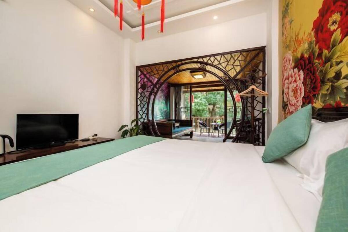 Un dormitorio con cama, televisión, escritorio y vistas a un espacio exterior con mesa y sillas.