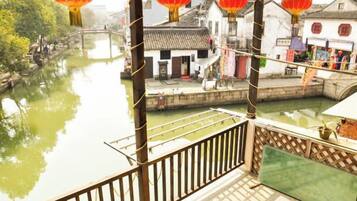 Um pátio tradicional chinês com varanda de madeira que dá para um canal, cercado por edifícios com telhados de cerâmica.
