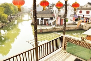 A traditional Chinese courtyard with a wooden balcony overlooking a waterway, surrounded by buildings with tiled roofs. - Shunshuiwan Inn (Suzhou)