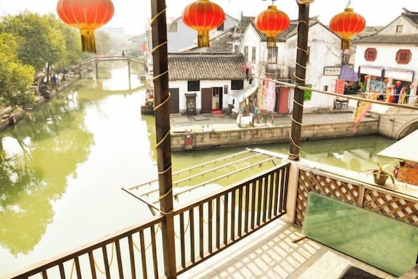 A traditional Chinese courtyard with a wooden balcony overlooking a waterway, surrounded by buildings with tiled roofs. - Shunshuiwan Inn (Suzhou)
