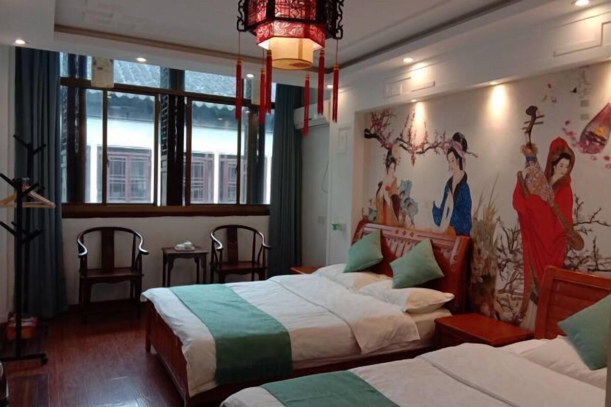 Habitación de hotel con dos camas, una ventana con cortinas, un cuadro en la pared y un farol colgante.