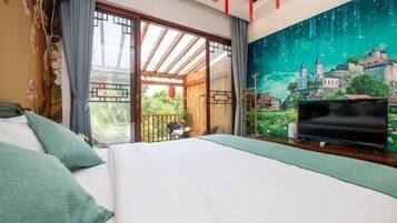 Una camera d'albergo con un letto grande, una televisione, un balcone che si affaccia sul verde e un murale raffigurante un borgo.