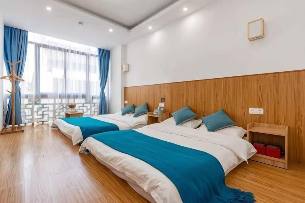 Habitación de hotel con dos camas, cabeceros de madera, piso de madera, una ventana con cortinas y una mesita de noche de madera con una lámpara.