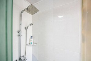 Une salle de bain avec des murs recouverts de carreaux blancs, une douche avec un pommeau de douche amovible et un distributeur de savon plac é sur une étagère.