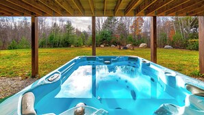 Una vasca idromassaggio sotto un gazebo in legno, con vista su un prato e alberi.