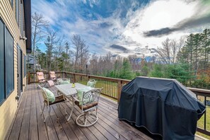Eine Holzterrasse mit Gartenmöbeln, einem Grill und Blick auf Bäume und Berge.