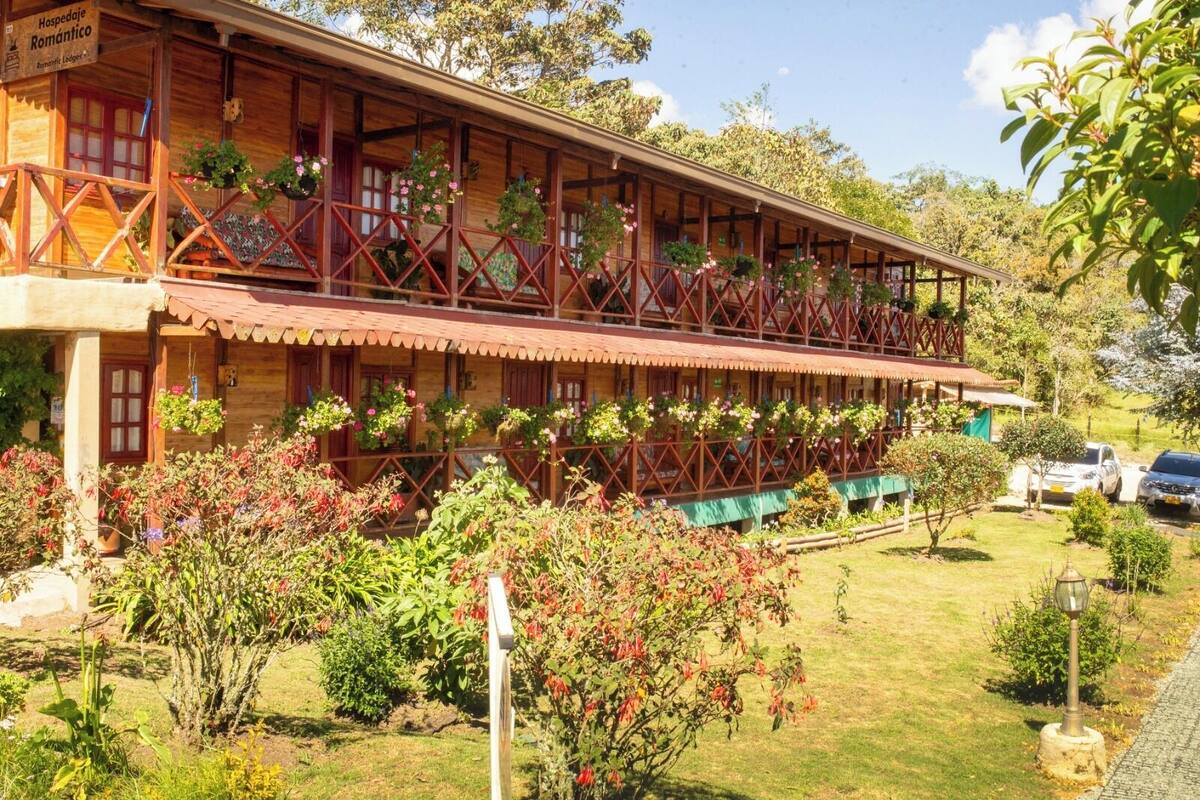 A two-story wooden building with balconies, surrounded by lush greenery and flowers.