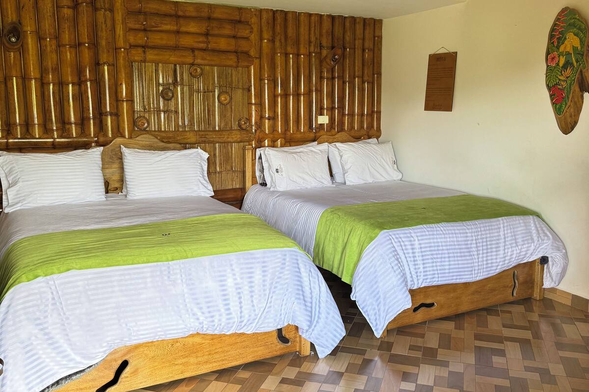 A room with two wooden beds, a bamboo headboard, a wooden floor, and a wall-mounted light fixture.