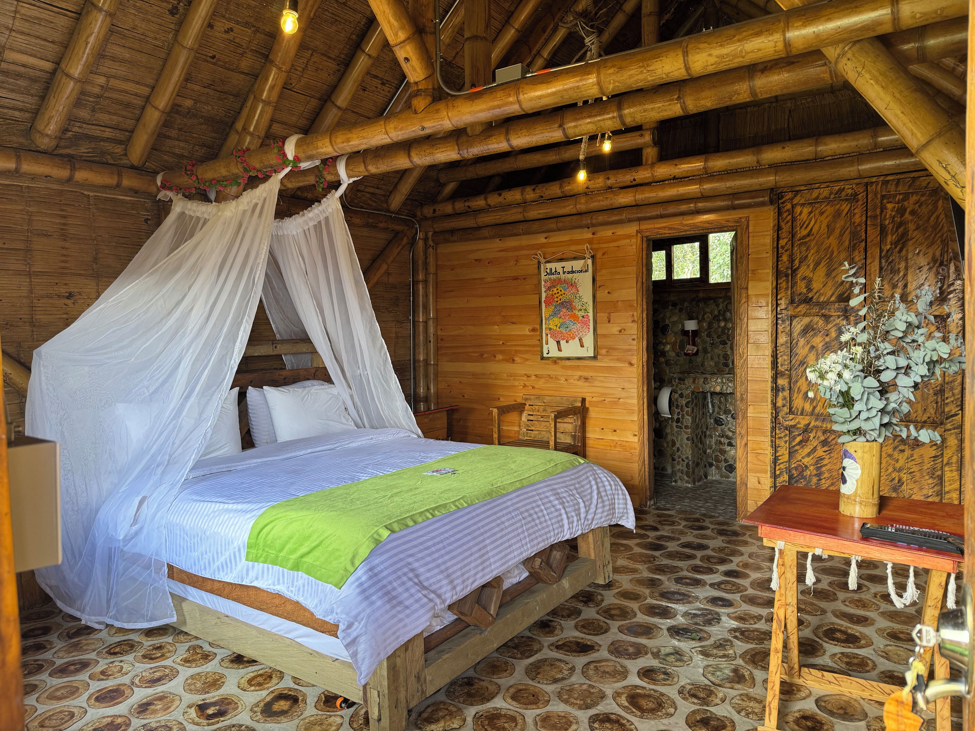 A rustic wooden room with a bed, a table, and a stone wall.