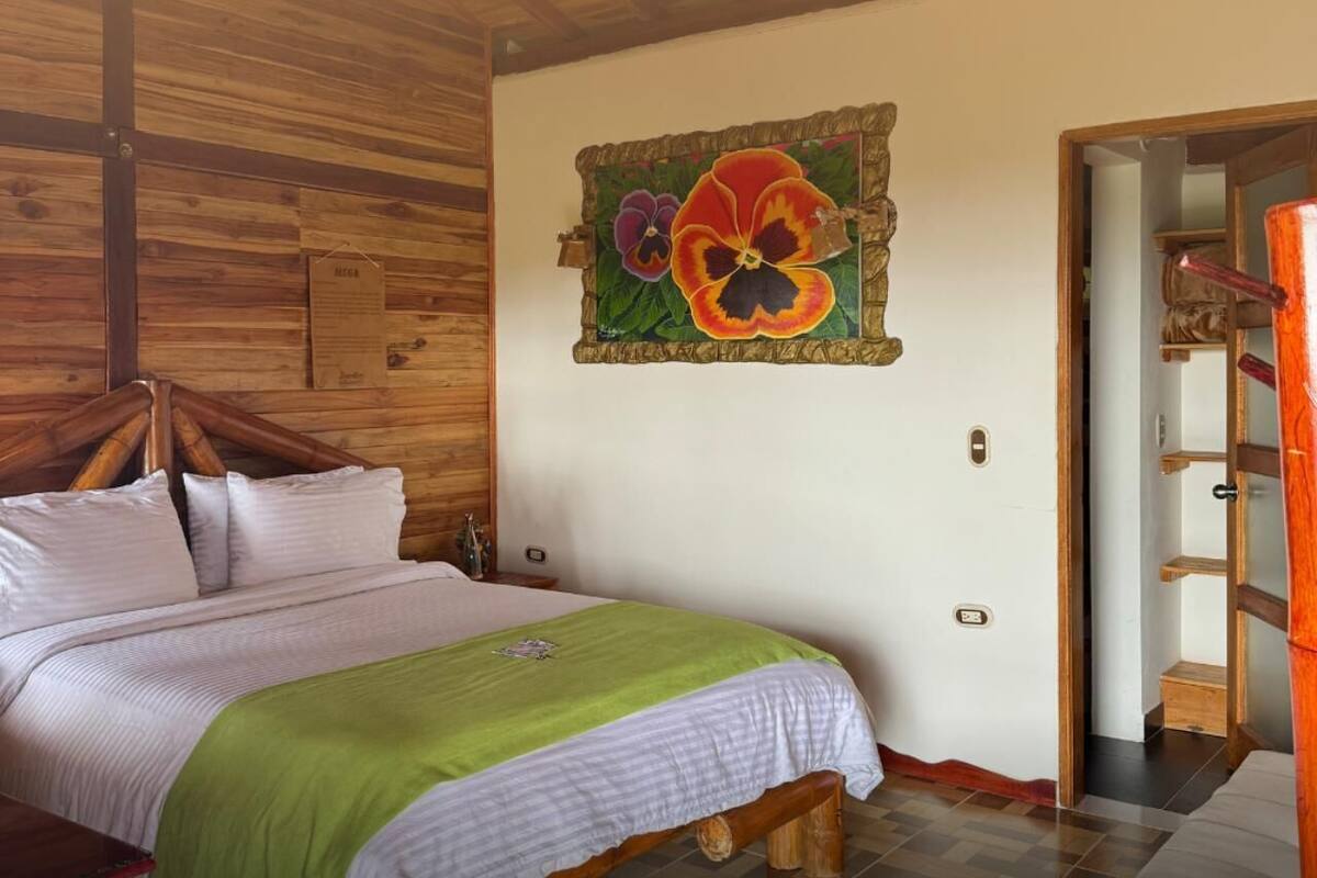 A wooden-paneled room with a bed, a green blanket, and a wall-mounted painting of flowers.