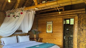 A wooden cabin bedroom with a bed, canopy, and a stone-walled bathroom. - Jardín de Silleteros Agro Parque Hotel (Envigado)