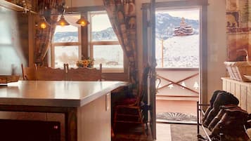 A kitchen with a large island, a dining area with chairs, a staircase leading to a balcony, and a view of mountains through a window.