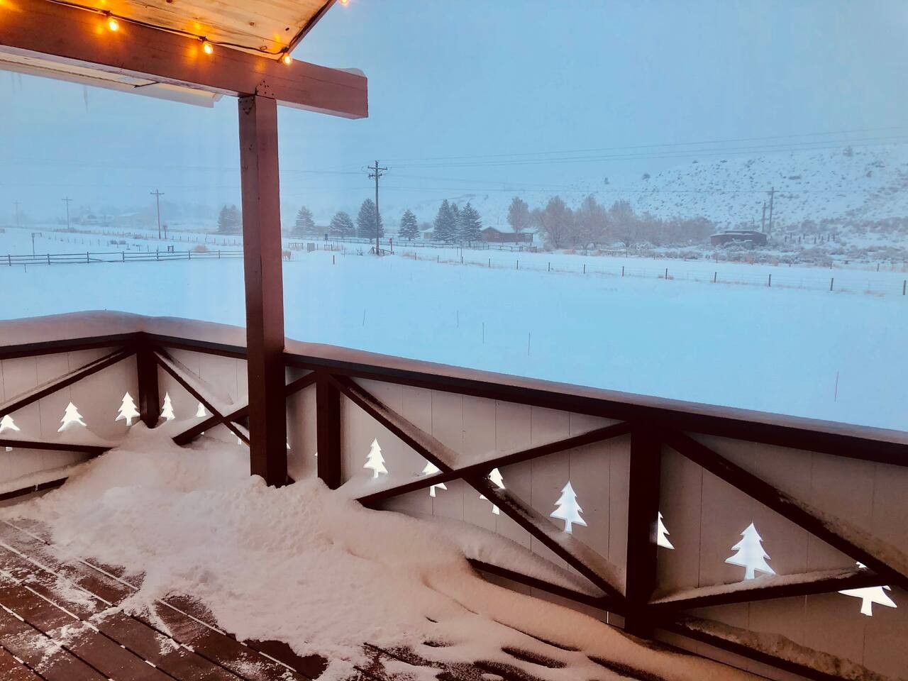 Ein verschneiter Außenbereich mit einer Holzterrasse und Blick auf eine verschneite Landschaft.