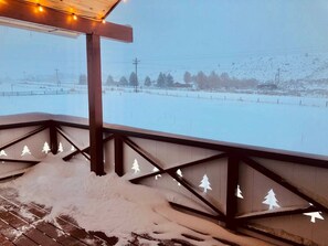 Un espace extérieur enneigé, doté d’une terrasse en bois et offrant une vue sur un paysage hivernal.