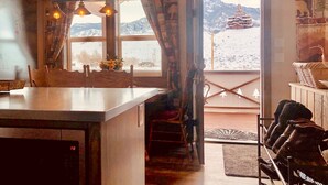 Una cucina con un'isola grande, una zona pranzo con sedie, una scala che conduce a un balcone e vista sulle montagne attraverso una finestra.