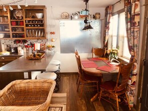 A cozy kitchen with wooden cabinets, a dining table with chairs, and a wicker chair.