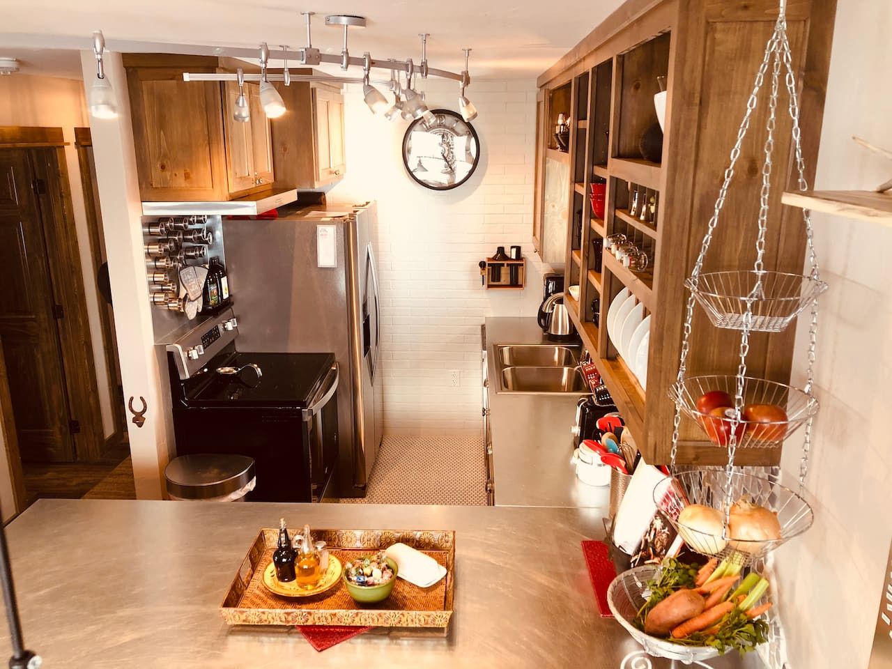 A compact kitchen with wooden cabinets, stainless steel appliances, and a hanging fruit basket.