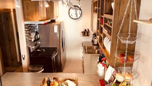 Una cucina compatta con mobili in legno, elettrodomestici in acciaio inox e un cesto appeso per la frutta.