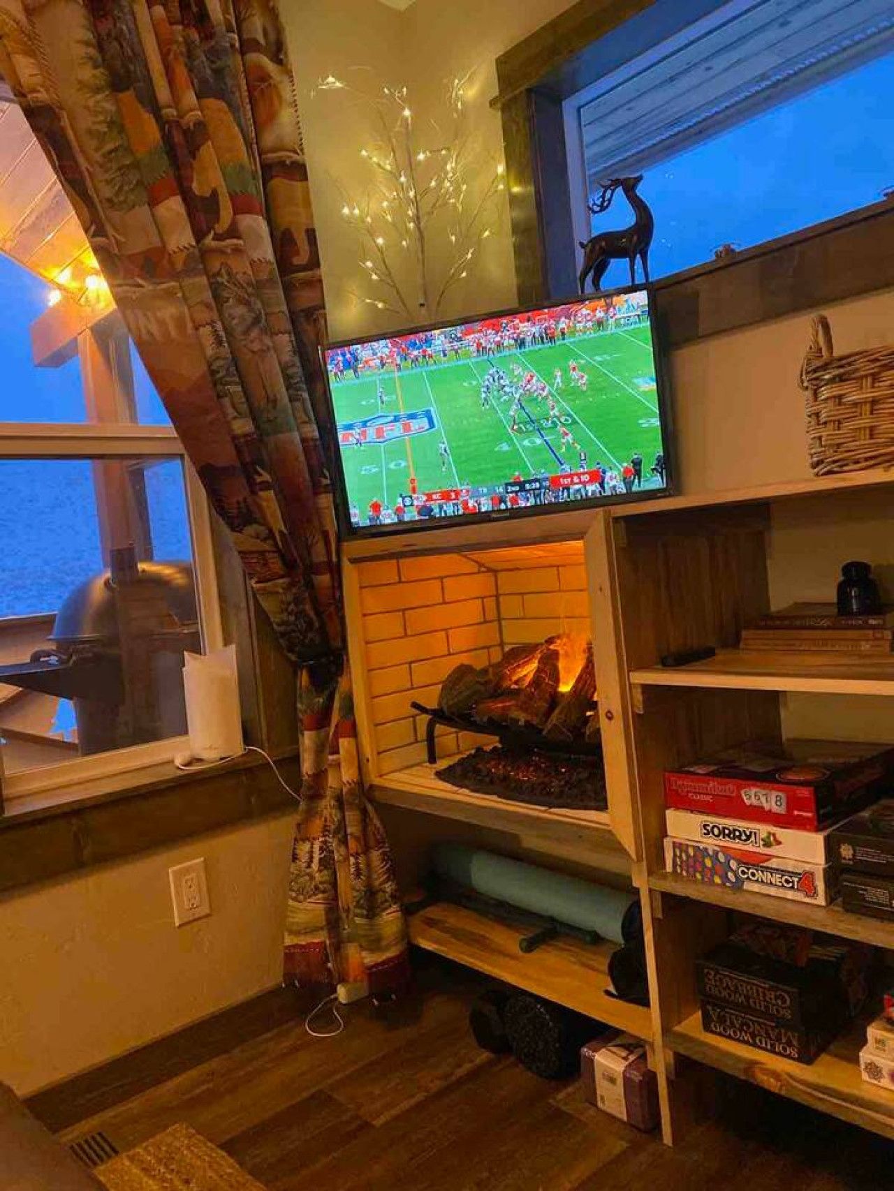 A living room with a television displaying a football game, a fireplace, and shelves with board games.