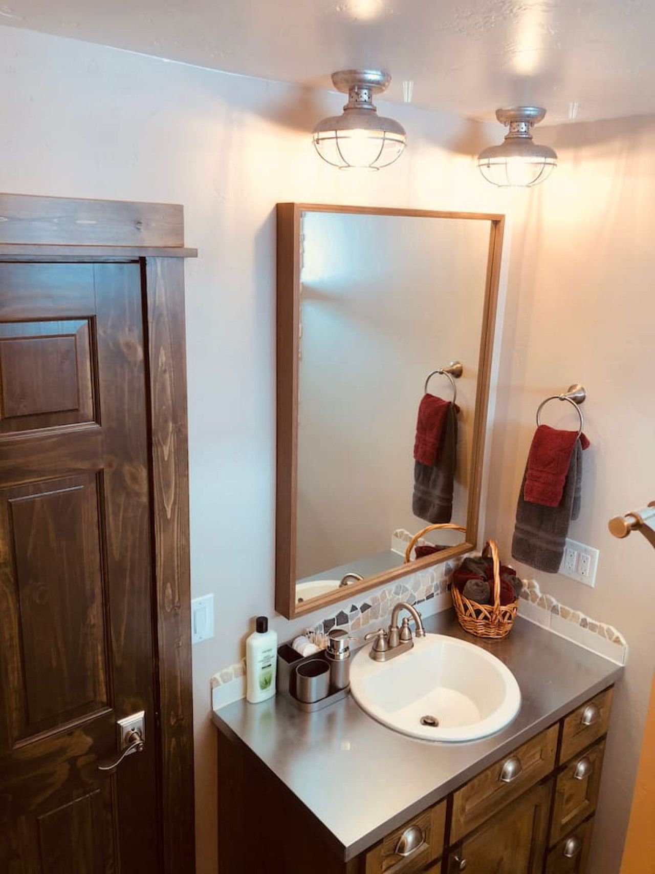 A bathroom with a wooden door, a large mirror, a sink with a faucet, and a towel rack.