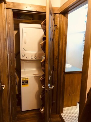 A laundry room with stacked washers and dryers, wooden doors, and a visible bathroom.