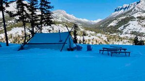 Un campamento cubierto de nieve con una tienda de campaña, una mesa de picnic y sillas.
