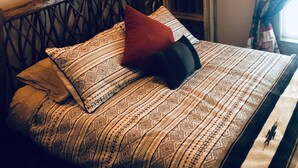 Una cama con ropa de cama estampada, cabecera y lámpara fijada a la pared.